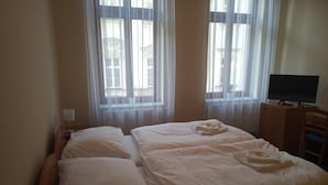 Ein Doppelbett mit weißen Bettwäsche, ein Nachttisch mit Lampe sowie ein Fernseher auf einer Holzkommode.