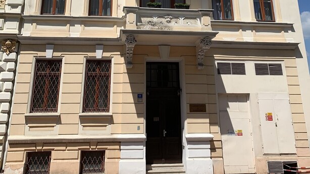 Ein mehrstöckiges Gebäude mit aufwendigen architektonischen Details, darunter Zierleisten und ein Balkon mit Blumentöpfen.
