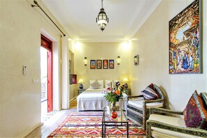 A hotel room with a bed, a sitting area with a chair and table, a decorative vase, and a painting on the wall. - Riad Tahyra (Marrakech)