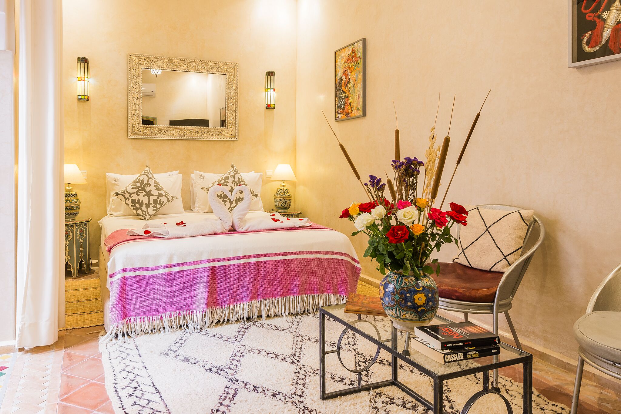 A hotel room with a bed, bedside tables, a chair, a coffee table, and a vase with flowers.