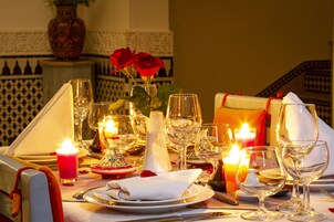 Una mesa dispuesta para una comida, con velas, copas y un jarrón con rosas rojas.