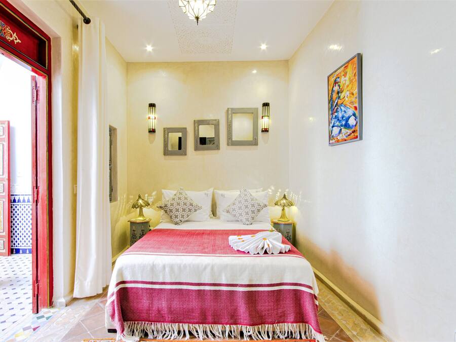 A hotel room with a bed, bedside lamps, a wall-mounted mirror, and a painting.