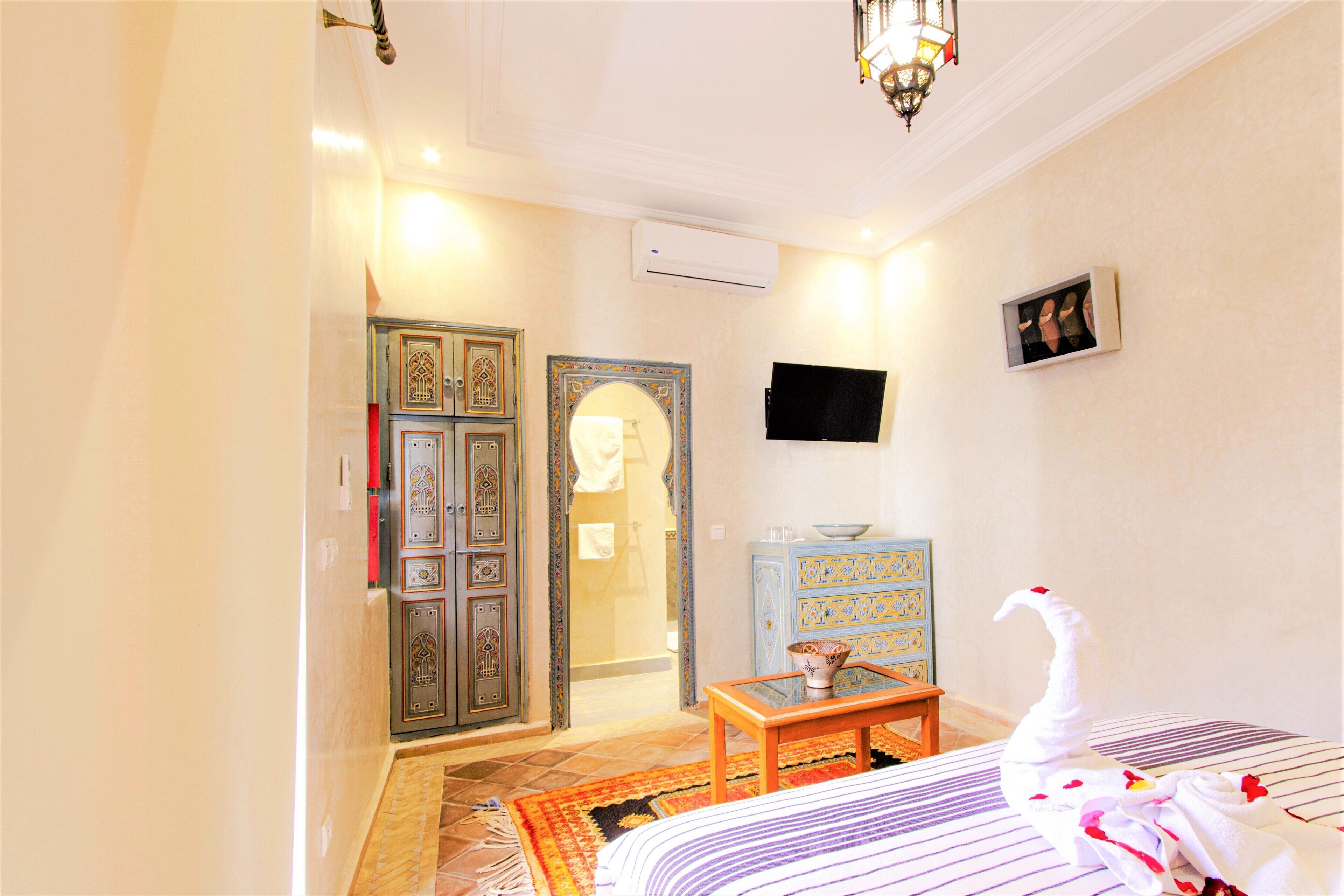 A hotel room with a bed, a small table, a TV, and a wardrobe.