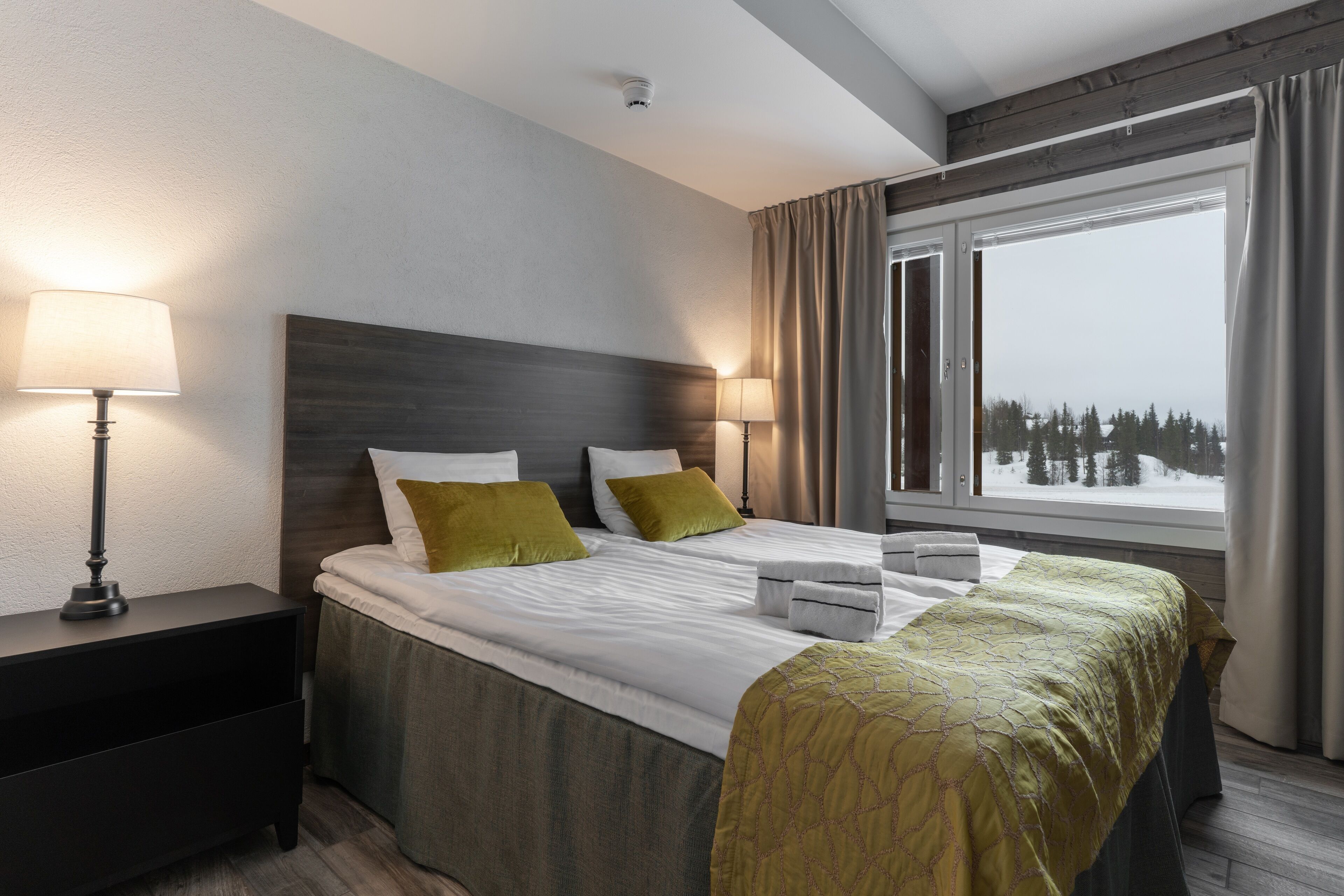 Una habitación de hotel con una cama grande, dos lámparas de noche, una mesita de noche y una ventana con cortinas.