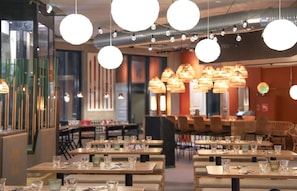 A modern restaurant interior with round pendant lights, wooden tables, and chairs.