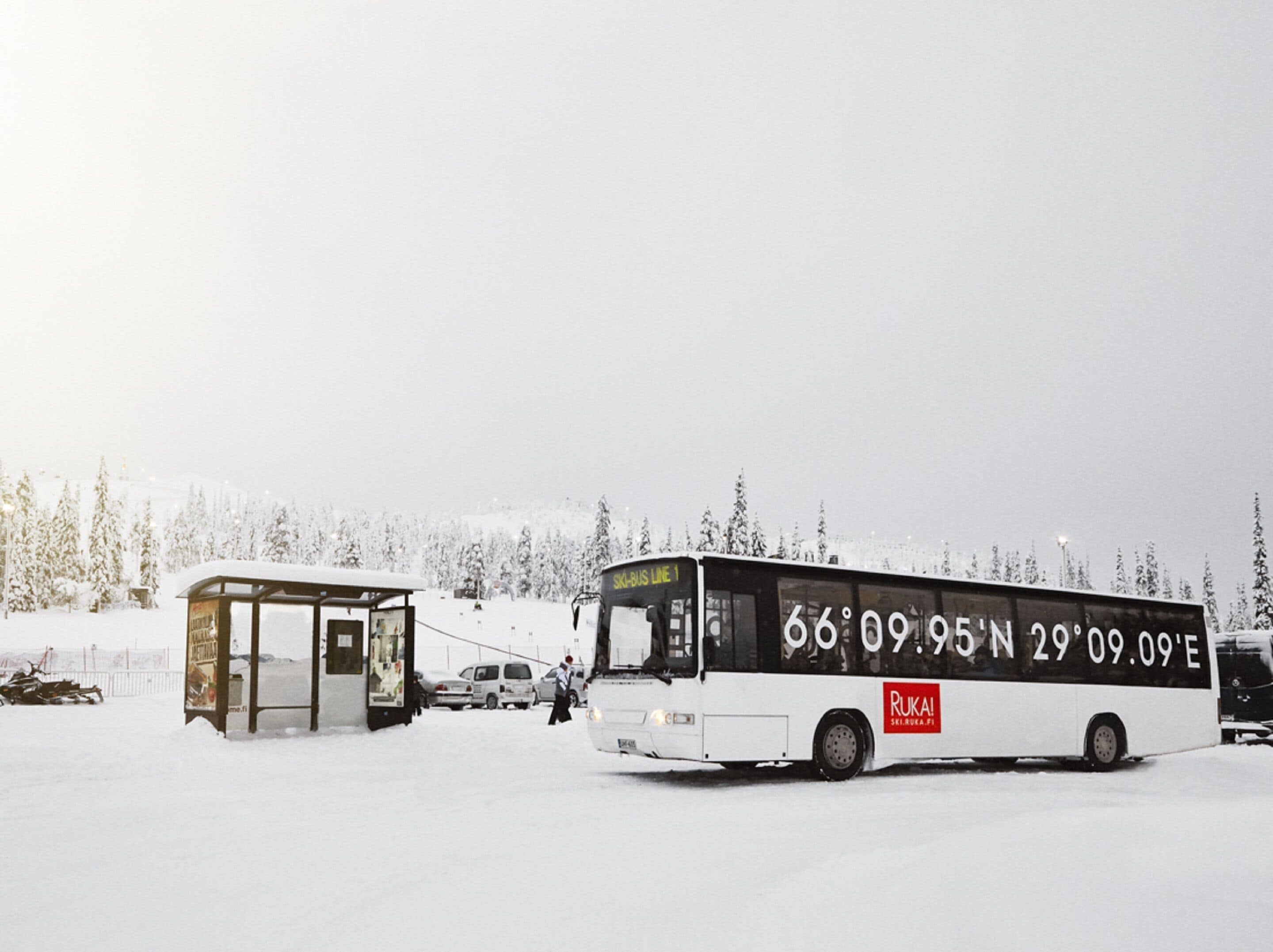 A bus at a bus stop in a snowy area with a sign displaying coordinates.