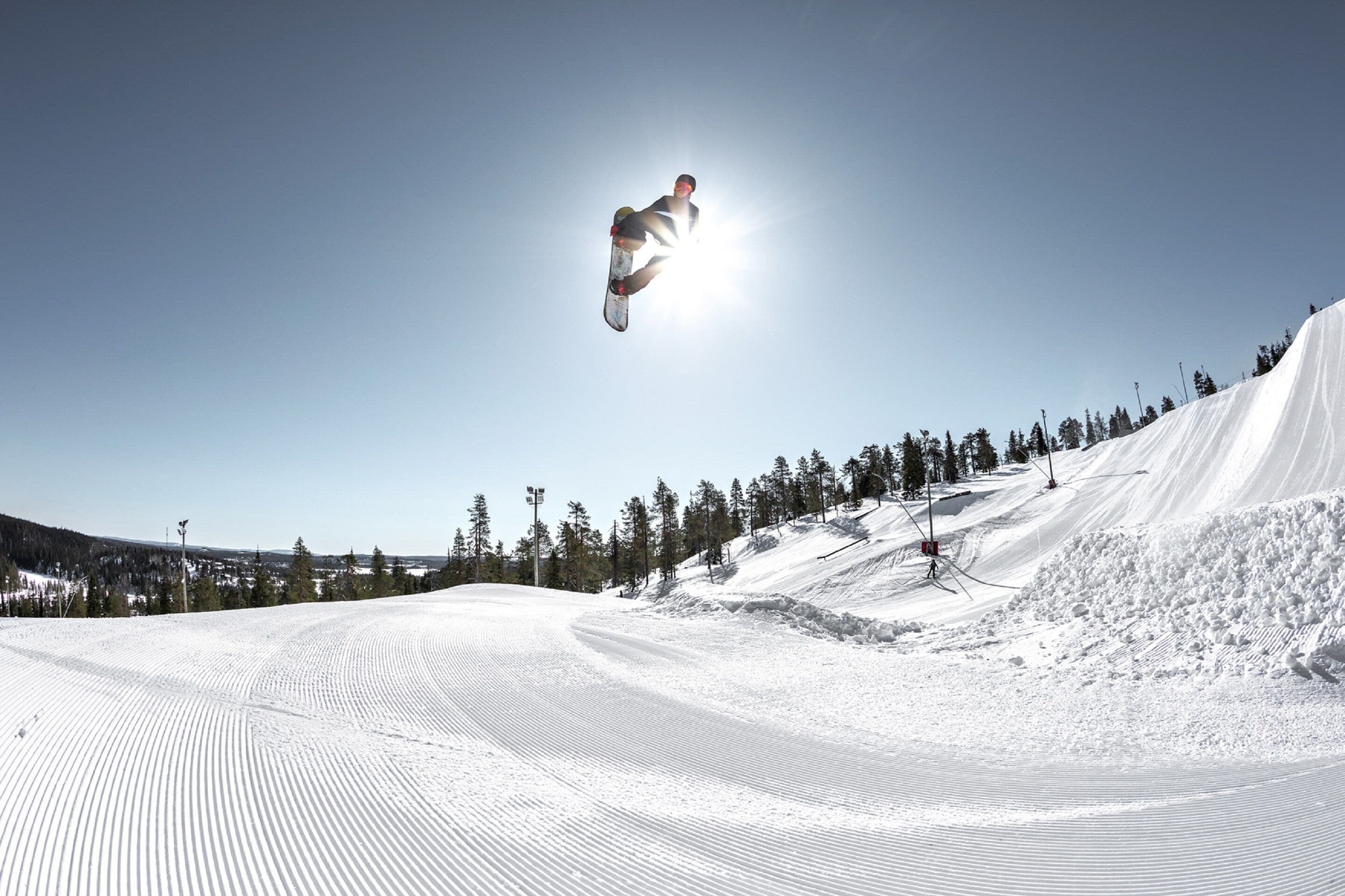 Un snowboarder realizando un salto en una ladera nevada bajo un cielo despejado.