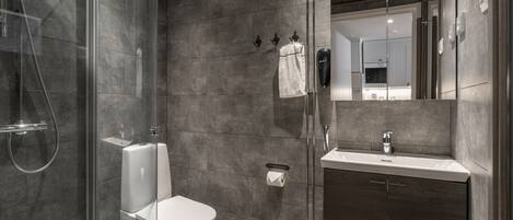 A modern bathroom with a glass-enclosed shower, a white toilet, a sink with a mirror, and a towel hanging on a rack.