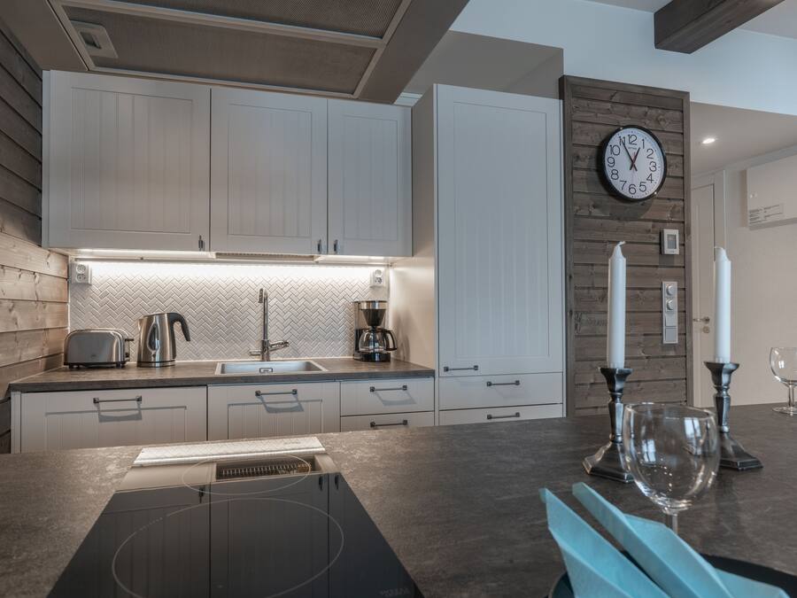 Una cucina moderna con mobili bianchi, forno integrato, macchina del caffè e orologio a parete.