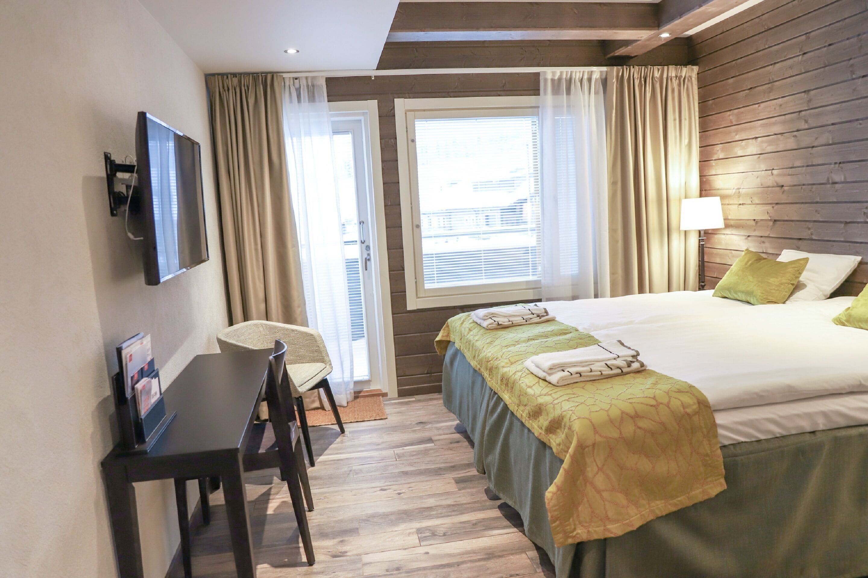 A hotel room with a bed, a desk, a chair, a TV, and a window with curtains.