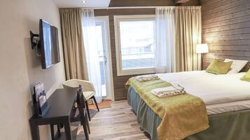 A hotel room with a bed, a desk, a chair, a TV, and a window with curtains.