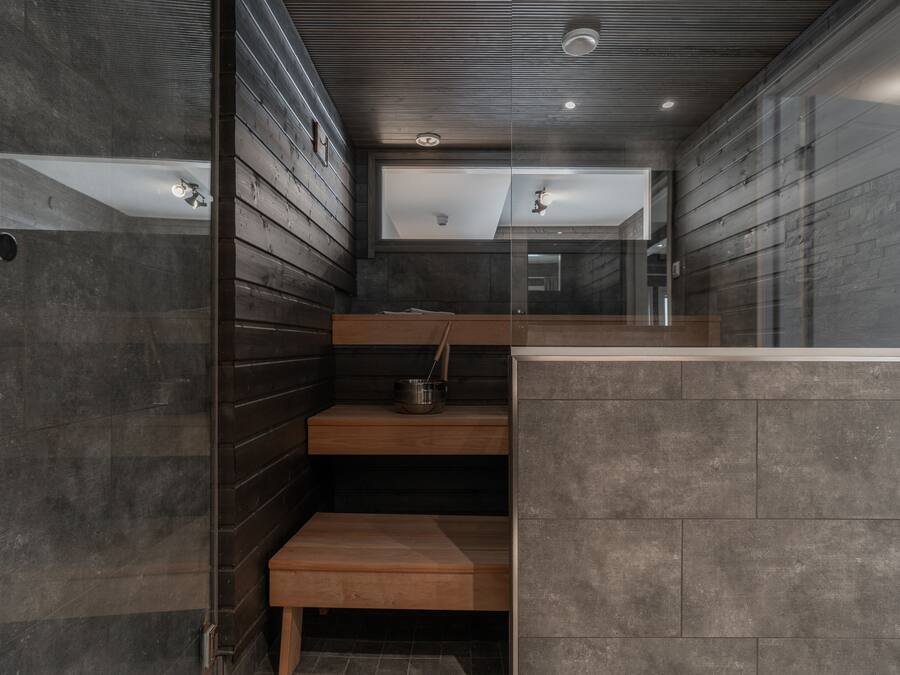 Ein modernes Badezimmer mit dunklen Steinwänden, Holzbanken und einer Glastrennwand.