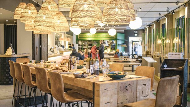 A restaurant with a long wooden table and multiple chairs, surrounded by hanging wicker lamps. - Ski-Inn RukaValley (Kuusamo)