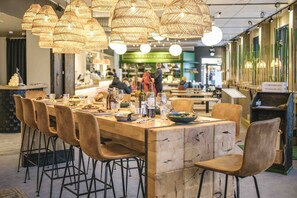 Um restaurante com uma longa mesa de madeira e várias cadeiras, rodeado por luminárias de vime suspensas.