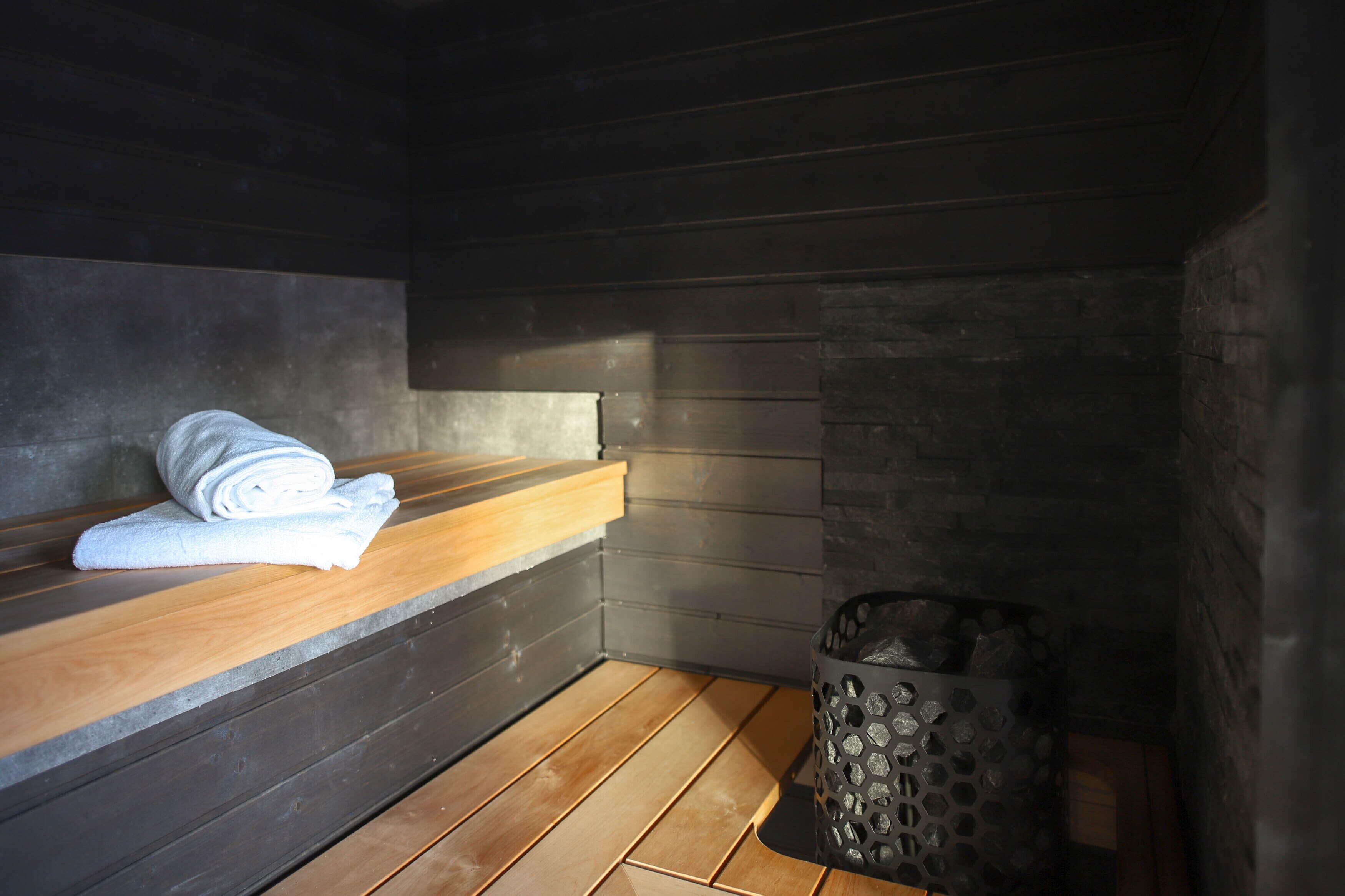 Uma sala de sauna com um banco de madeira, uma toalha e uma parede de pedra.