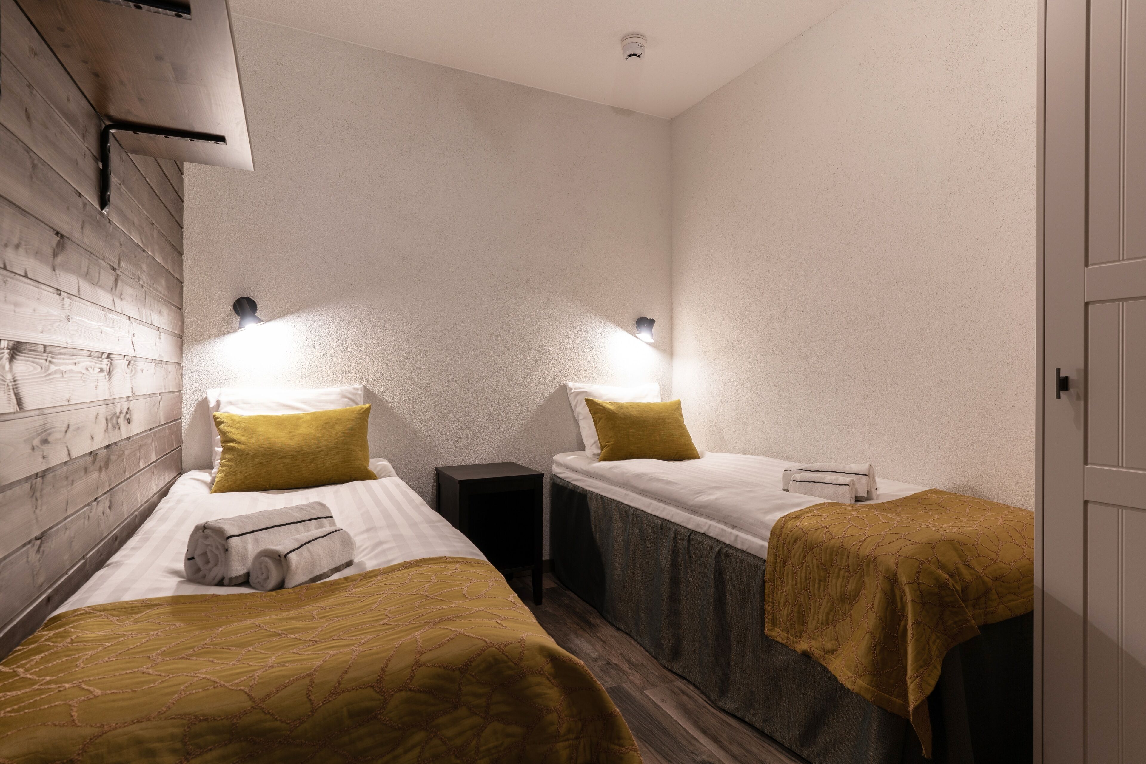 A room with two beds, each with a headboard, a nightstand, and a wall-mounted light fixture.