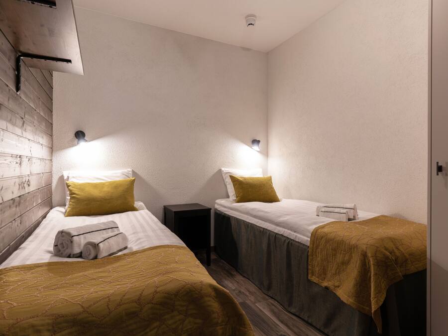 A room with two beds, each with a headboard, a nightstand, and a wall-mounted light fixture.