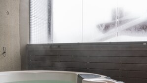 A hot tub with a wooden surround, a window with blinds, and a concrete wall. - Ski-Inn RukaValley (Kuusamo)
