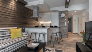 A modern kitchen with white cabinets, a wooden accent wall, and a built-in island with bar stools. - Ski-Inn RukaValley (Kuusamo)