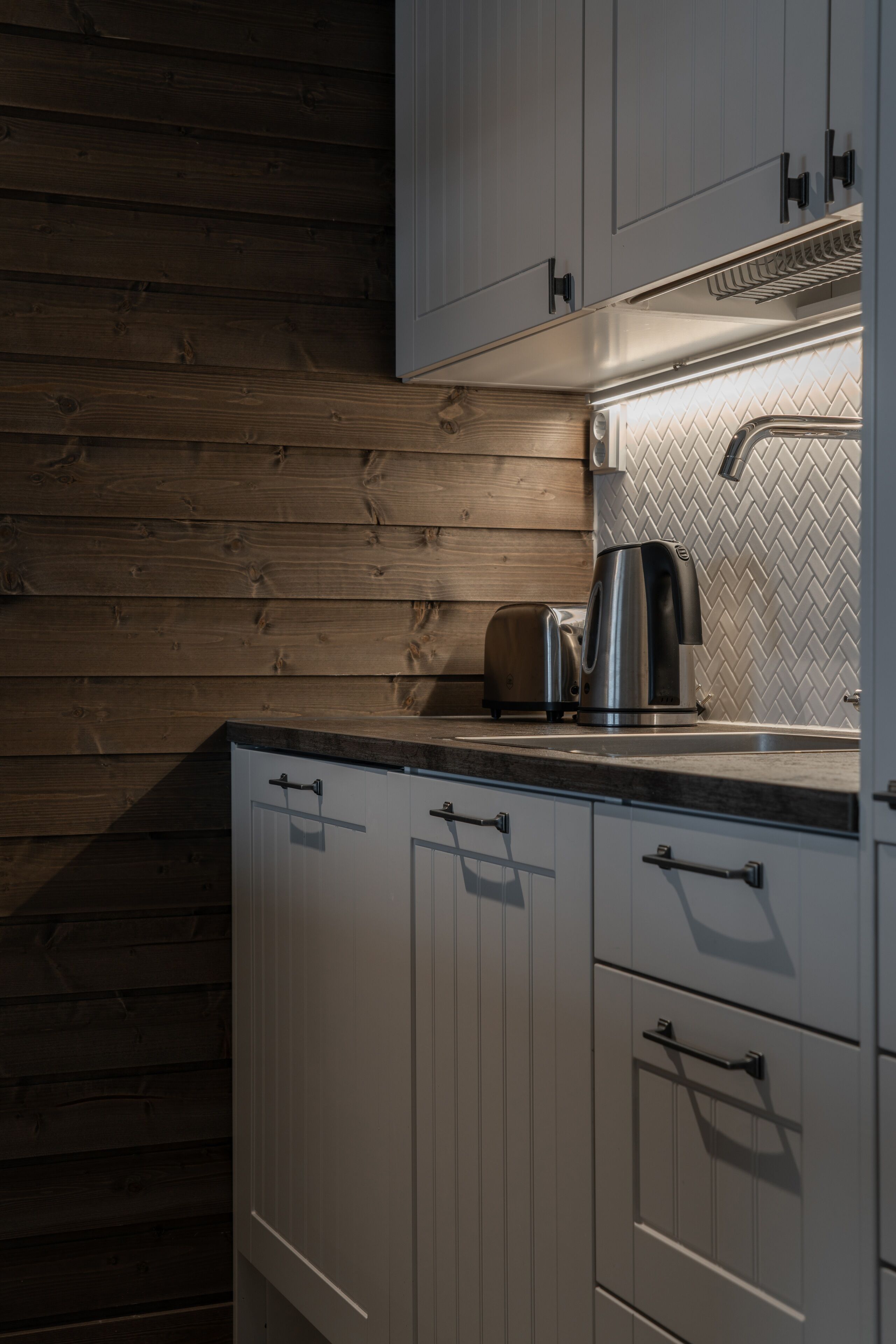 Una cocina con paneles de madera, una tetera y un tostador sobre la encimera.