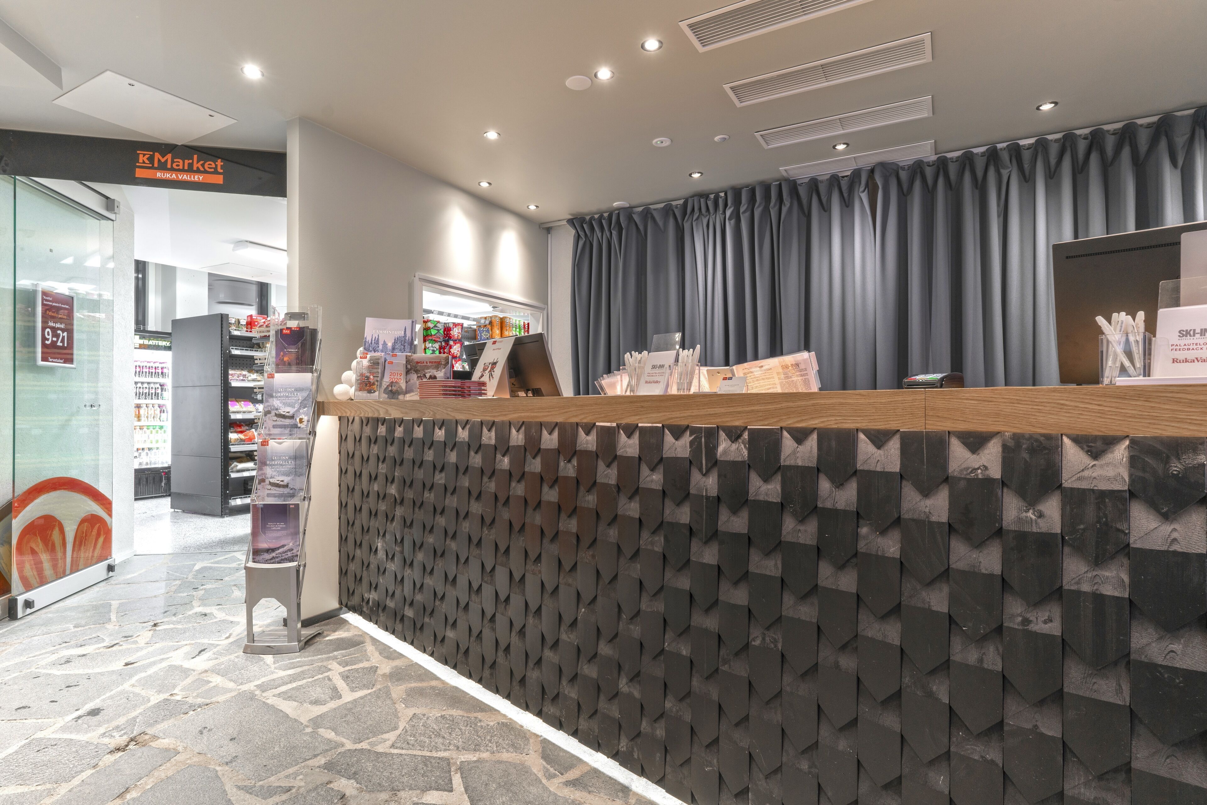 A reception desk with a patterned wall, a counter with informational brochures, and a store in the background.