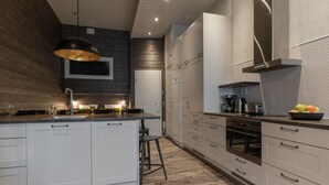 A modern kitchen with white cabinetry, a central island, a hanging light fixture, and a stainless steel range hood. - Ski-Inn RukaValley (Kuusamo)