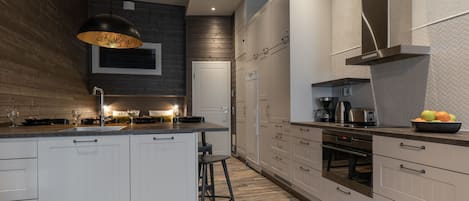 A modern kitchen with white cabinetry, a central island, a hanging light fixture, and a stainless steel range hood.
