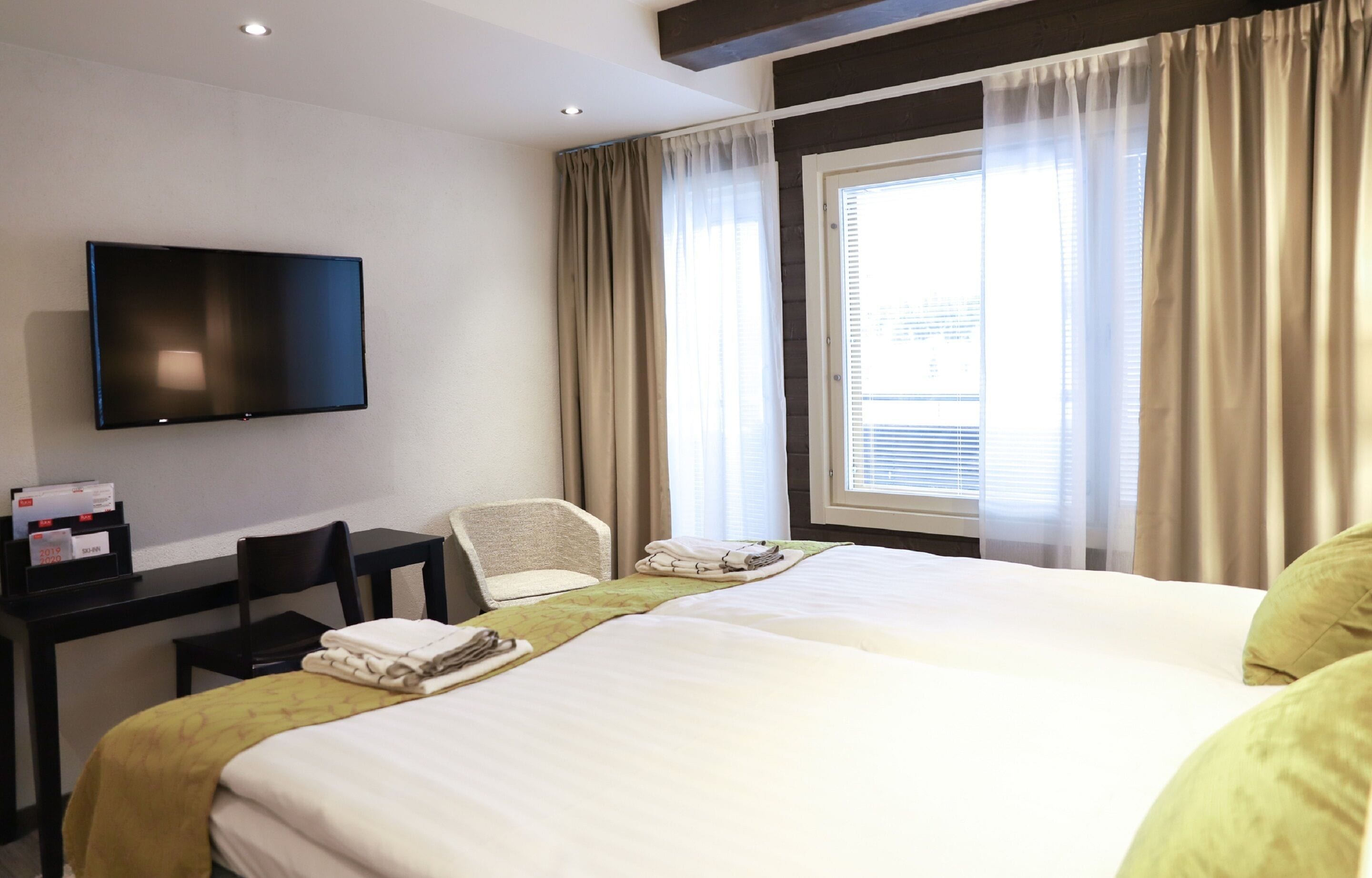 A hotel room with a bed, a desk, a chair, a television, and a window with curtains.