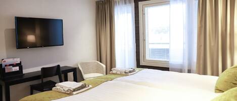 A hotel room with a bed, a desk, a chair, a television, and a window with curtains.