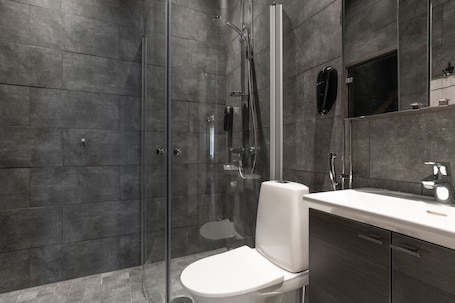 A modern bathroom with a glass-enclosed shower, a white toilet, and a dark-toned vanity with a mirror.