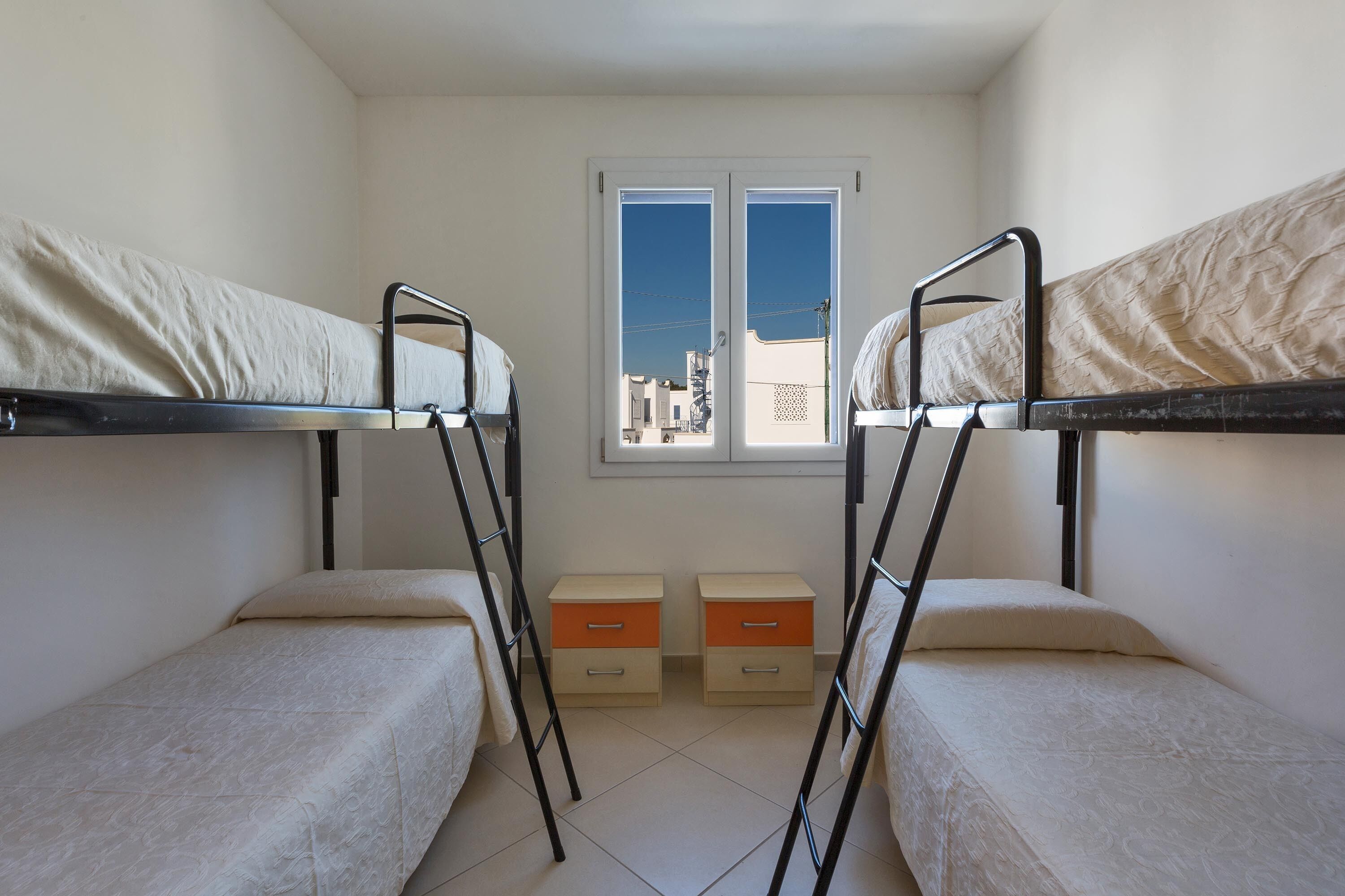 A dormitory room with bunk beds, a window, and two bedside tables.