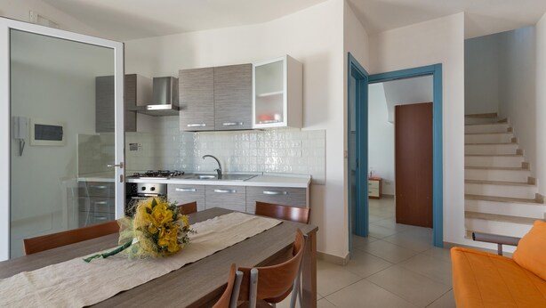 A modern kitchen with a dining area, a staircase, and a view of the living room. - Villetta Catia (Nardò)
