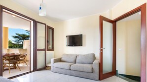 A living room with a sofa, a flat-screen TV mounted on the wall, and a sliding glass door leading to an outdoor area with a dining table and chairs. - Villetta Lucri (Nardò)