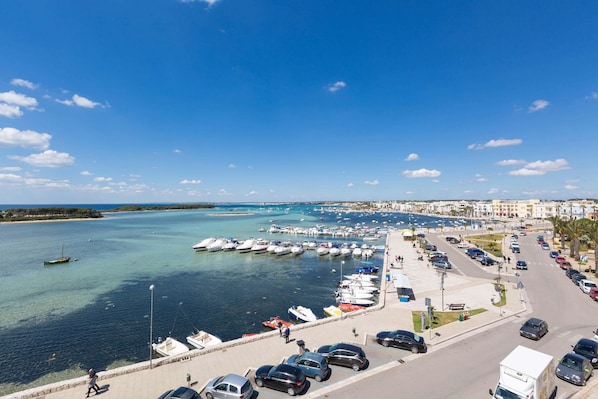 A marina with boats docked, a parking area with cars, and a clear blue sky.