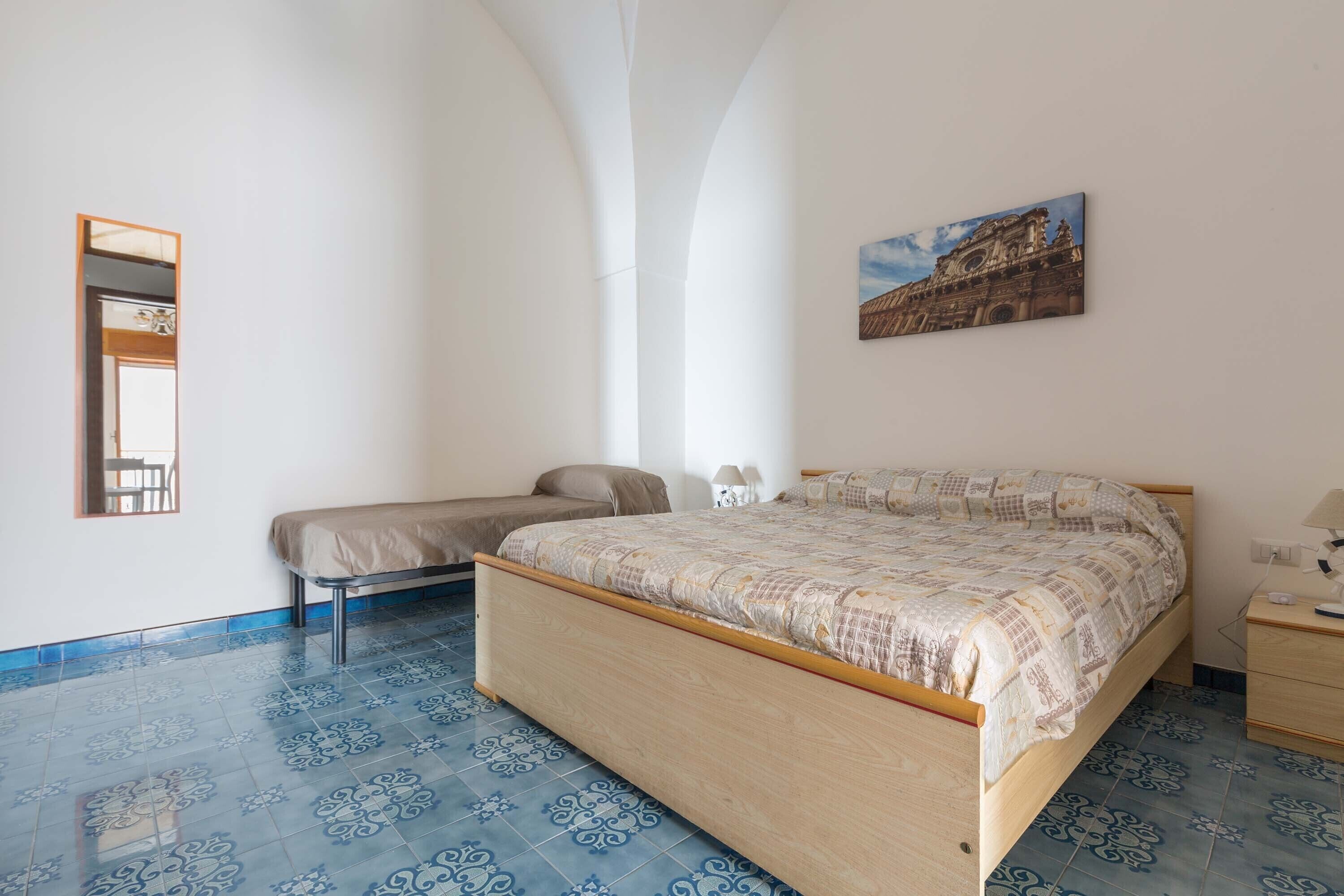 Ein Schlafzimmer mit einem großen Bett, einem Einzelbett, einem Nachttisch, einem Spiegel und einem Wandbild.