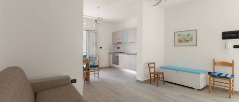 Un salon moderne comprenant un canapé, une table à manger avec des chaises, un coin cuisine avec des placards et un banc bleu.