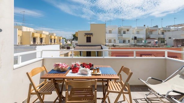 A balcony with a table set for dining, chairs, and a lounge chair.