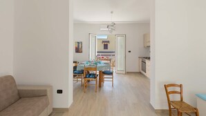 A modern living room with a sofa, a dining area with a table and chairs, and a kitchen in the background.