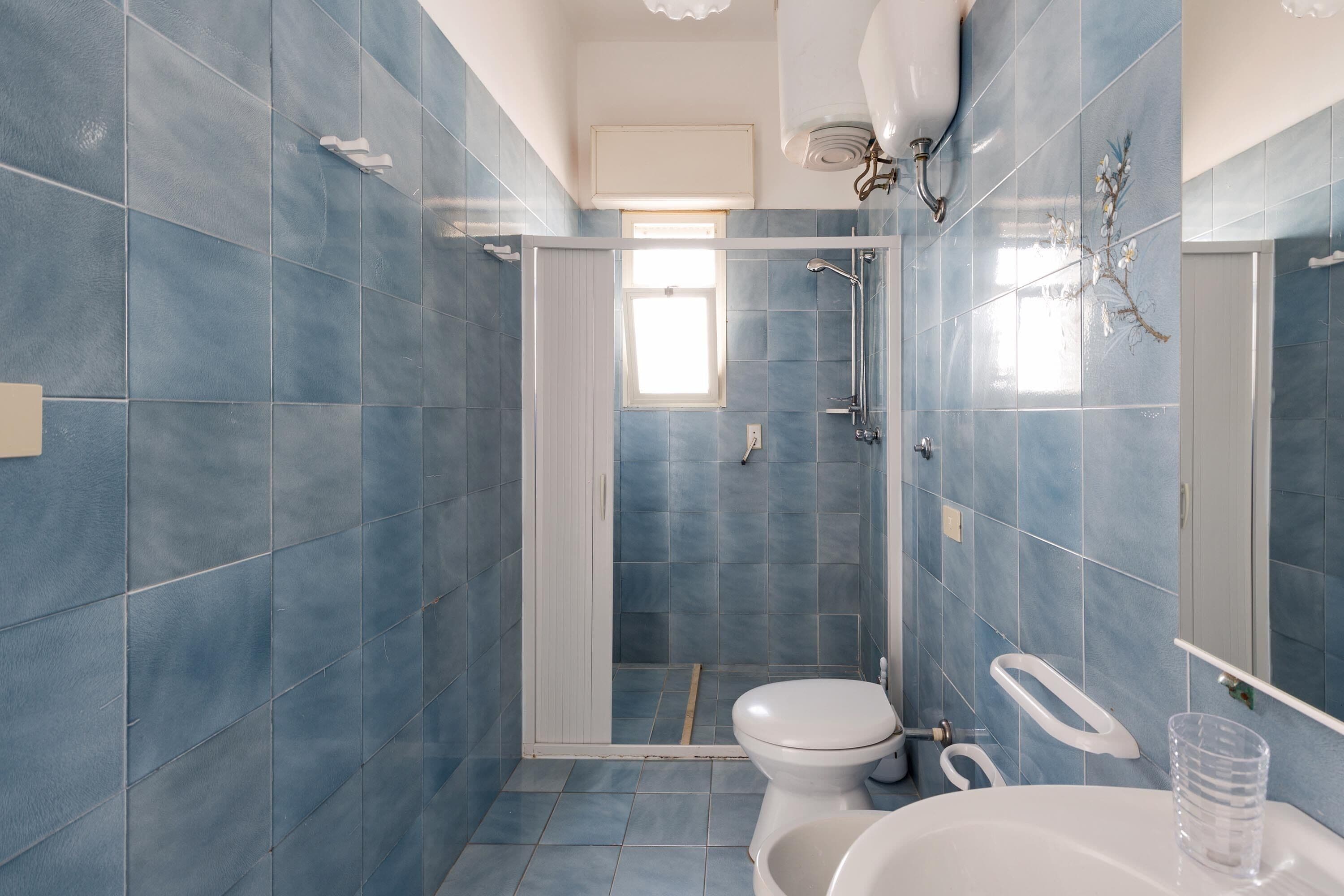 Une salle de bain avec des carreaux bleus, des toilettes, une douche et un lavabo.