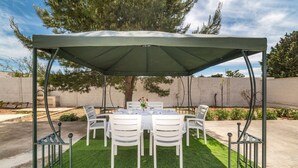 A covered outdoor dining area with a table and chairs, surrounded by a low wall and trees. - Villa Melograno (Porto Cesareo)