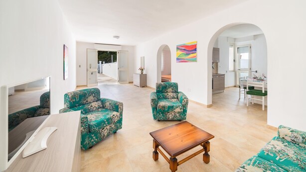 A spacious living area with a sofa, armchairs, and a coffee table. There are archways leading to other rooms and a kitchen area visible in the background. - Villa Melograno (Porto Cesareo)