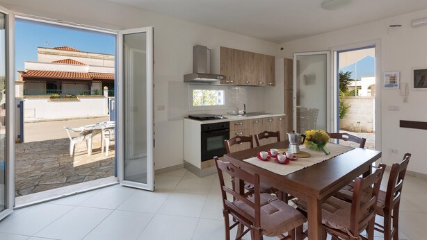 A modern kitchen with a dining area, large windows, and a view of the outside. - Villetta Raffaele (Nardò)