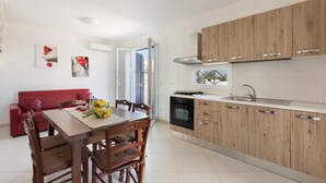 A modern kitchen with wooden cabinets, a built-in oven, and a sink. There is a dining area with a red sofa and wooden table. - Villetta Raffaele (Nardò)