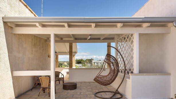 Un patio couvert avec des fauteuils en osier, un fauteuil suspendu et une vue sur le ciel.