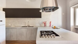 Une cuisine moderne dotée d’un îlot central, d’une hotte de cuisine en acier inoxydable et d’un luminaire suspendu.