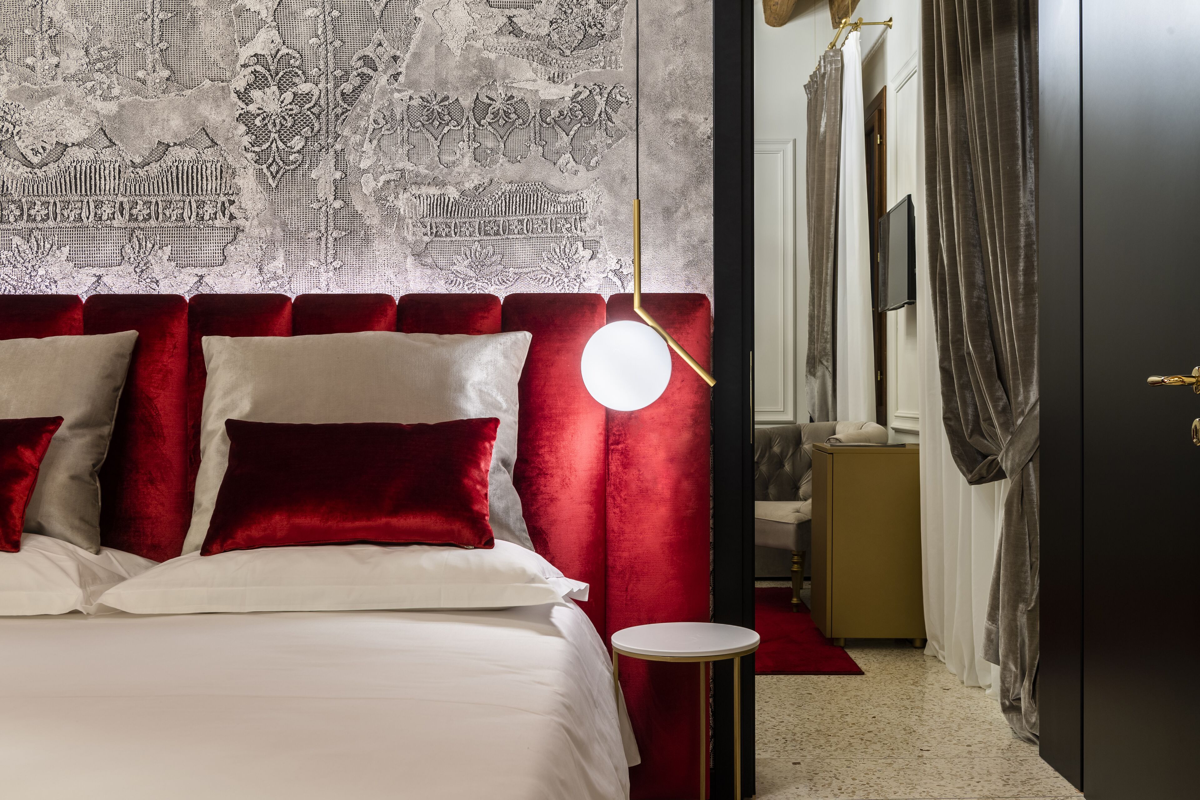 Habitación de hotel con una cama grande, cabecera de terciopelo rojo y una lámpara de pared redonda.