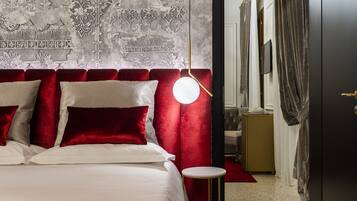 Habitación de hotel con una cama grande, cabecera de terciopelo rojo y una lámpara de pared redonda.