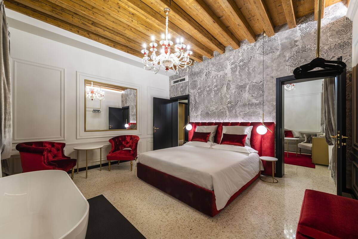 Une chambre spacieuse avec un grand lit, des fauteuils à revêtement rouge, une baignoire blanche et un lustre.