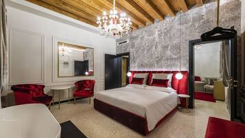 Une chambre spacieuse avec un grand lit, des fauteuils à revêtement rouge, une baignoire blanche et un lustre.