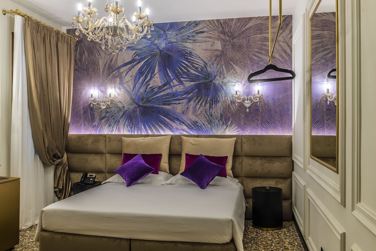 Une chambre à coucher avec un grand lit, un lustre, un téléphone et un mur orné d’un motif de feuilles tropicales.